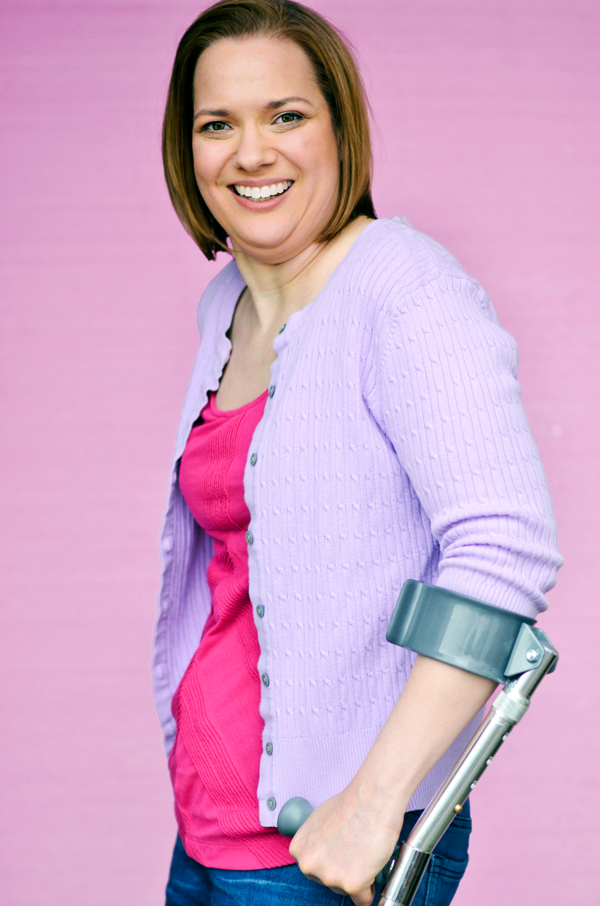 Dawn Grabowski medium headshot, side profile, smiling at the camera. She is standing with forearm crutches in a lilac sweater over a pink shirt and jeans.