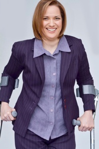 Dawn Grabowski with smile on her face, standing with forearm crutches. She is wearing a purple suit jacket, and lilac dress shirt.