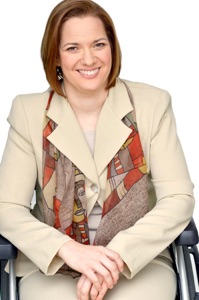 Dawn Grabowski in a beige suit jacket wearing a scarf under the collar. She is sitting in a wheelchair.