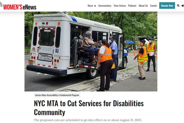 Small white bus with wheelchair access parked along a street as bus driver helps load passenger in wheelchair.